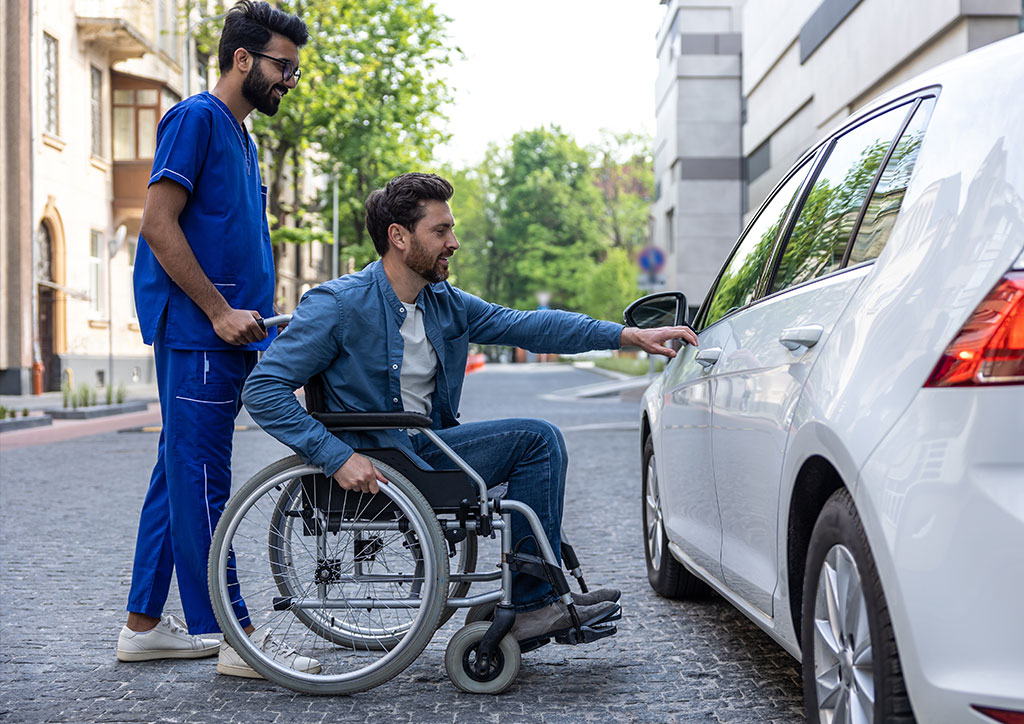 Helfer f&auml;hrt Rollstuhlfahrer im eigenen Auto zu Termin