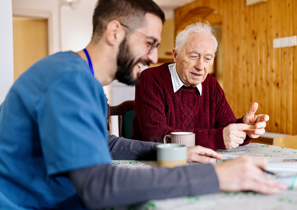 Pflegemitarbeiter in mobiler Pflege h&auml;lt Gespr&auml;ch mit Senior im h&auml;uslichen Umfeld